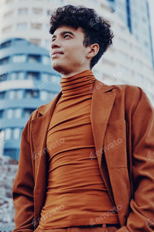 Preview: Young man in a stylish brown outfit with a turtleneck smiles confidently against a modern urban