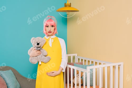 Preview: retro styled pregnant pin up woman with pink hair holding teddy bear in child room