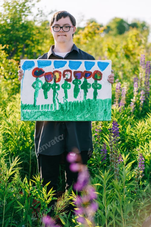 Preview: Child with Down syndrome showing flower painting in meadow