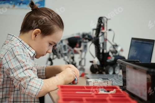 Preview: Smart schoolboy sitting at the table and constructing a robotic device