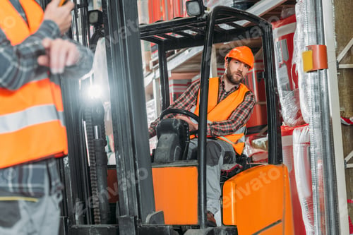 Preview: worker in safety vest and helmet sitting in forklift machine in storage