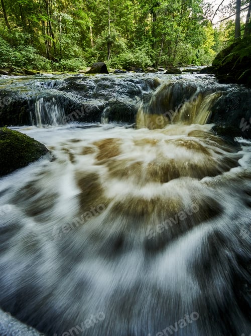 Preview: Scenic ivew of a river flowing through a lush forest with trees and rocks