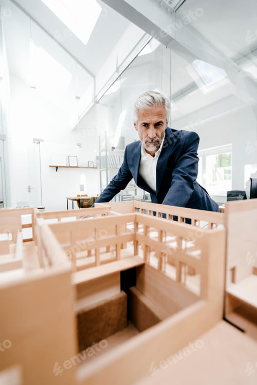 Preview: Mature businessman examining architectural model in office