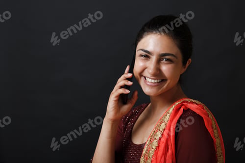 Preview: Portrait of smiling young adult indian woman in sari talking mobile phone