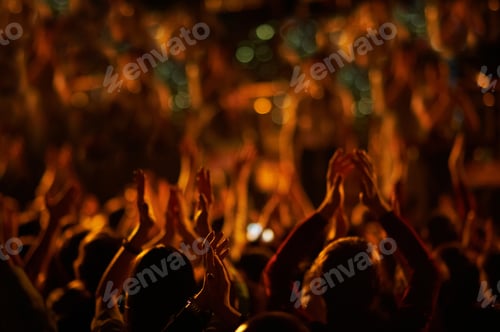 Preview: Audience with hands raised at a music festival and lights streaming down from above the stage.