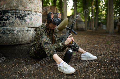 Preview: Female paintball player sitting on the ground