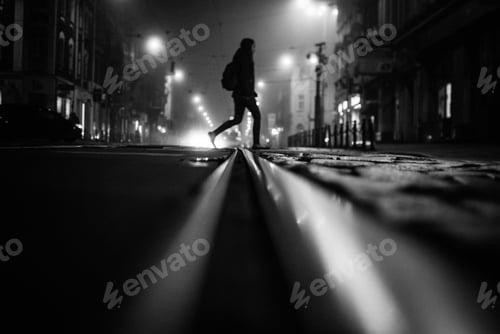 Preview: Grey scale shot of a person crossing the street at night