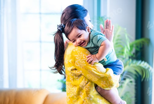 Preview: Indian Mom gently holding sleeping infant boy on shoulder, bonding quietly in bright modern home