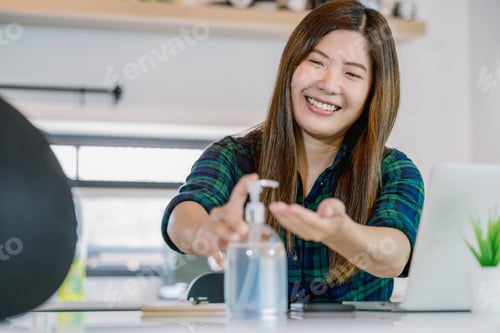 Preview: Asian woman using hand sanitizer when working at home with technology laptop