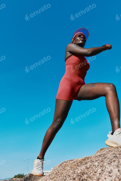 Preview: Young woman standing confidently on a rock against a clear blue sky, showcasing strength and