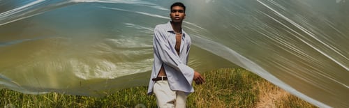 Preview: young african american man in trendy summer outfit near cellophane film in field, banner