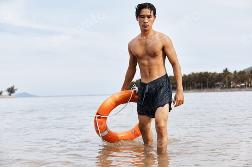 Preview: Alert Asian Lifeguard watching over joyful swimmers on the sandy beach, ensuring safety and rescue