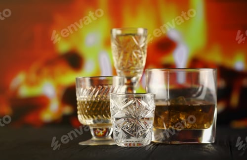 Preview: Different alcohol drinks in glass on wooden surface on fireplace background