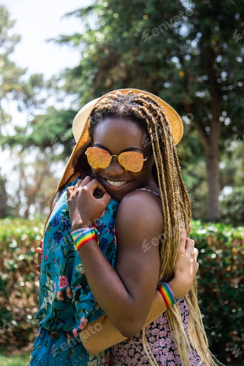 Preview: Portrait of multiracial couple of gay women hugging in the park. Vertical image.