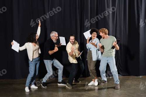 Preview: overjoyed multiracial theater troupe holding clipboards with screenplays and showing success