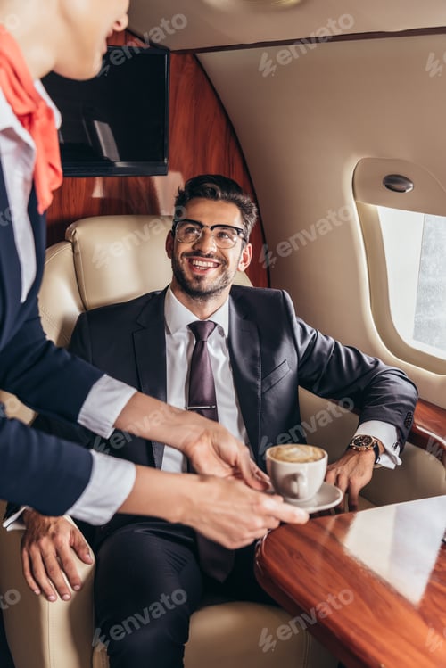 Preview: cropped view of flight attendant giving cup of coffee to handsome businessman in suit in private