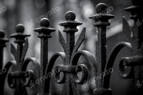 Preview: Low angle greyscale view of a rusty metallic fence with a spider web on it on a blurry background