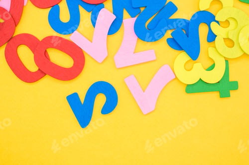 Preview: Flat lay of colorful wooden numbers on a yellow surface - space for text