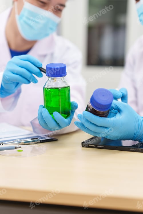 Preview: Two Asian scientists in lab coats sit at table in laboratory, examining samples through microscope