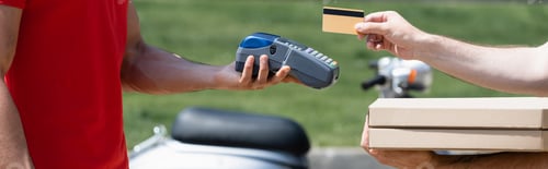 Preview: Cropped view of man with pizza boxes holding credit card near courier with payment terminal