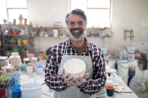 Preview: Proud male potter showing his creation to camera in the pottery workshop
