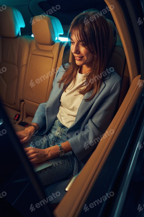Preview: Joyful woman riding in car and using laptop