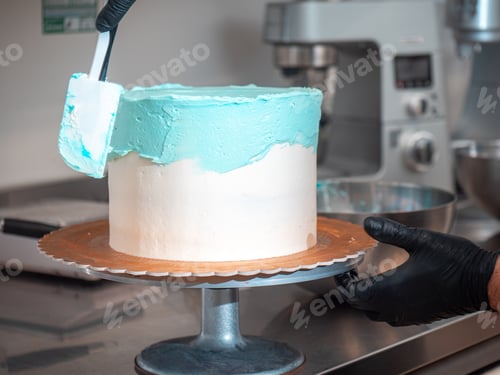 Preview: cake designer covering a frosted blank cake with turquoise light blue cream with spatula