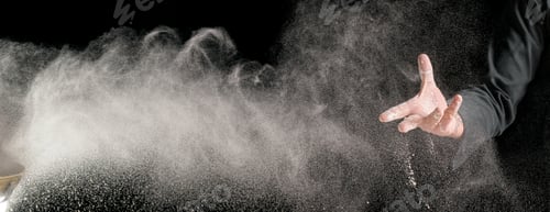 Preview: Hand of professional cook sprinkles flour, flour flies in the form of a cloud