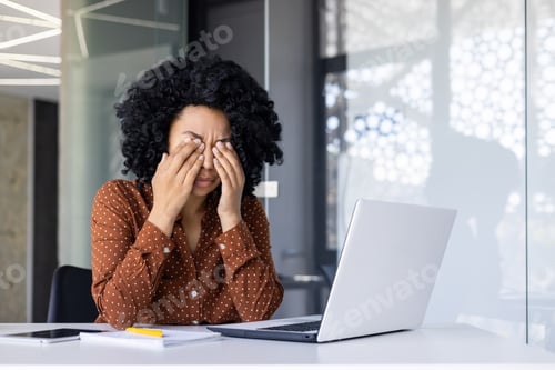 Preview: Tired woman with curly hair working at desk experiencing stress and fatigue during work