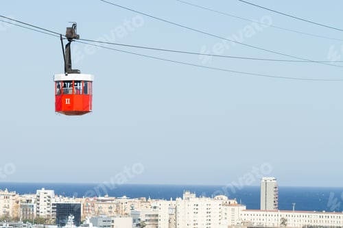 Preview: Closeup shot of a red cable car in Barcelona with the background of a city, sea, and the sky