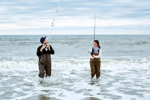 Preview: Young couple in waders sea fishing knee deep in water