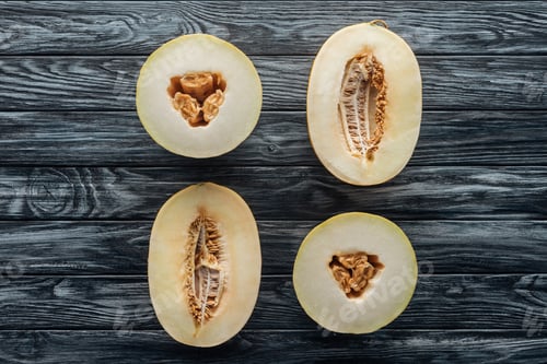 Preview: top view of halved ripe sweet honeydew and cantaloupe melons on wooden surface