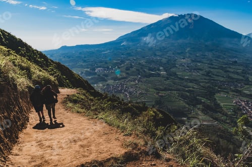 Preview: two people walking down the mountain with the view of a big mountain in front of them