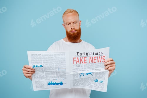 Preview: skeptical bearded man reading newspaper with fake news, isolated on blue
