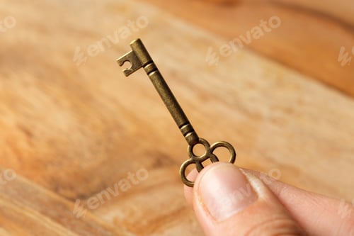Preview: Unique decorative key held between fingers on wooden surface