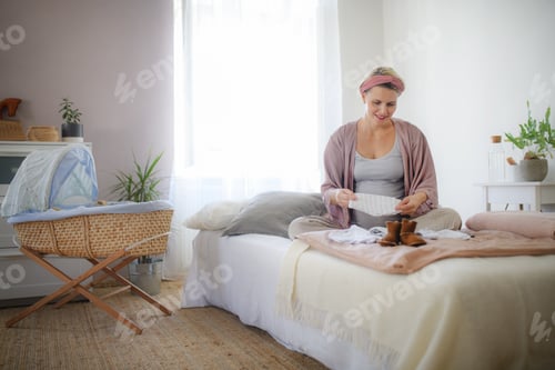 Preview: Happy pregnant woman looking at little clothes for her baby.