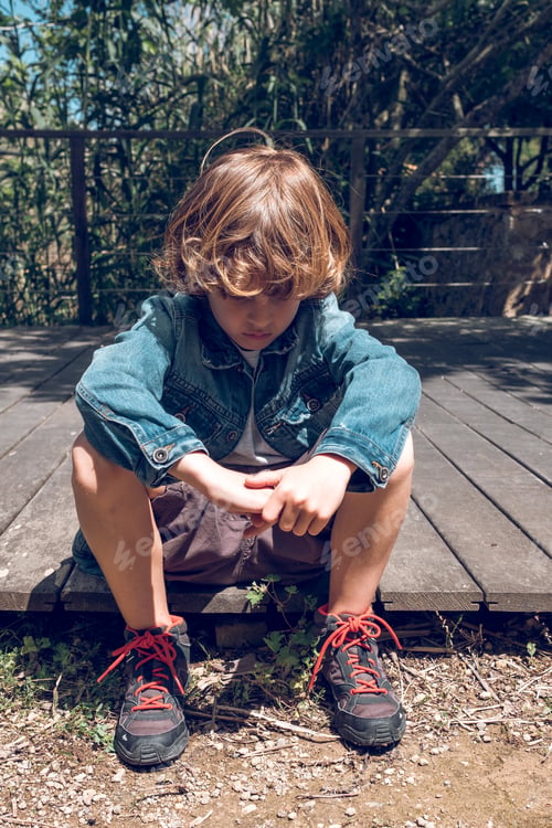 Preview: Sad preteen boy sitting on wooden boardwalk
