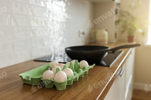 Preview: White chicken eggs in green cardboard egg tray on tabletop at modern stylish kitchen. Black frying