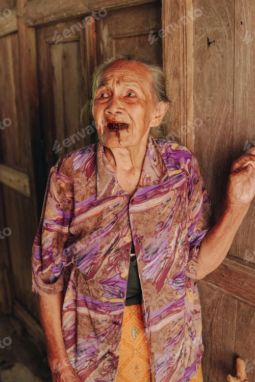 Preview: Senior elderly woman wearing purple kebaya, traditional Indonesian clothes, standing by the door.