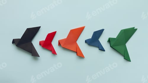 Preview: five paper origami pigeons black, red, orange,blue and green in row on light background