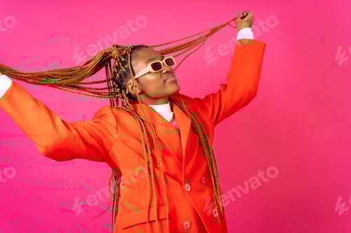 Preview: African young woman with braids on a pink background, in a red suit having fun and dancing