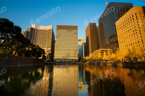 Preview: Buildings surrounded by vibrant golden autumn trees, under a clear blue sky with warm sunlight high