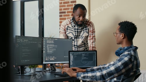 Preview: Software developer sitting at desk with multiple screens and laptop running code