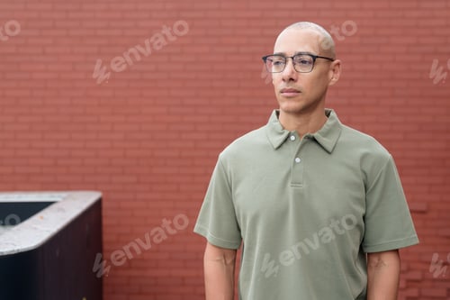 Preview: Hispanic bald man in polo shirt outdoors against brick wall