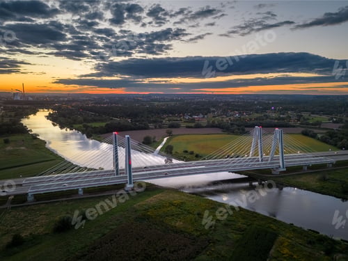 Preview: Aerial view of a long bridge spanning a wide river at sunset in a rural setting