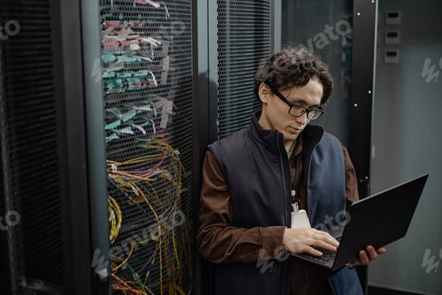 Preview: Young Adult Asian Man Using Laptop While Working Inside Server Room