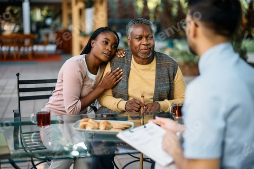 Preview: Black senior man and his daughter communicating with healthcare worker on patio at care home.