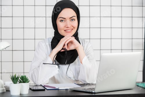Preview: A Muslim Doctor smiling with glasses and stethoscope and documents on a white office background