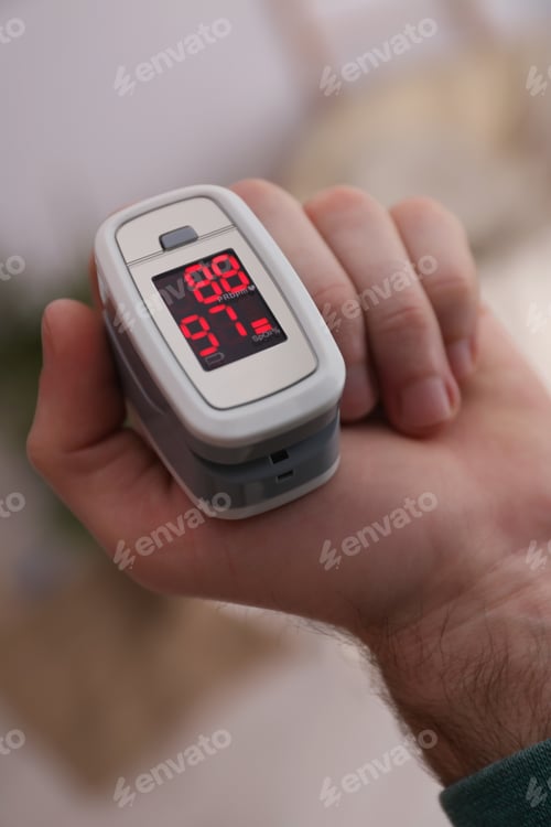 Preview: Man measuring oxygen level with modern fingertip pulse oximeter indoors, closeup