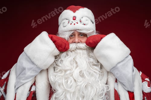 Preview: father frost in long warm coat, red mittens and a hat touches his moustache and smiles